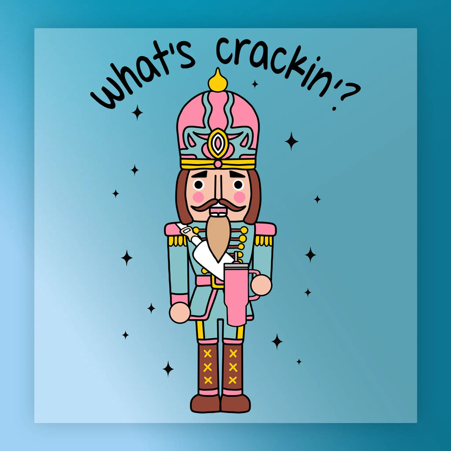 The Nutcracker Soldier Christmas Design by InkMerge showcases a vibrant cartoon soldier in uniform with "what's crackin?" above, surrounded by black stars on a blue gradient—ideal for festive heat press transfer projects.