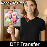 A woman holding a colorful watercolor painting of a soccer ball with a heart on it, and there is a red arrow pointing to her chest.