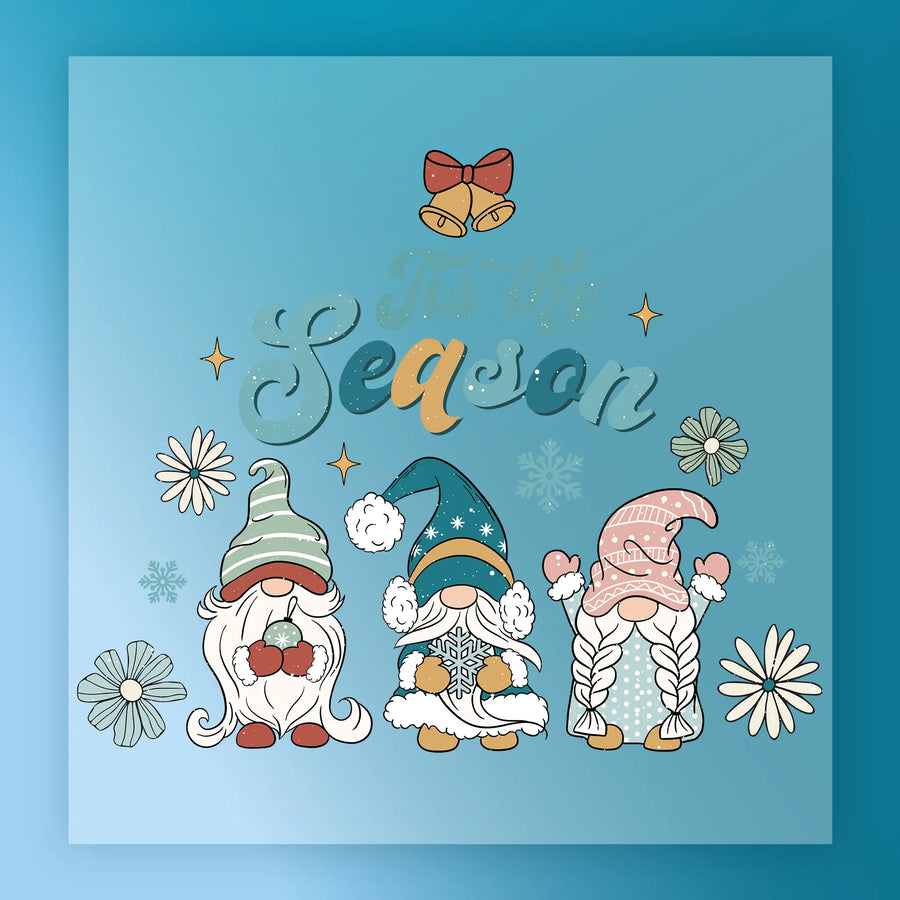 Three festive gnomes with flowers and snowflakes stand under “’Tis the Season” on a blue, starry background. The InkMerge Tis the Season Gnome Design is heat press ready—perfect for your next project!.