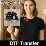 A smiling woman in a black shirt holds an InkMerge Camp Hair Don't Care Design - Heat Press Ready DTF transfer sheet, showing a camper, pine tree, and sun with "Ready To Press Direct-to-Film transfer" text above.