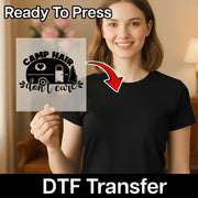A smiling woman in a black shirt holds an InkMerge Camp Hair Don't Care Design - Heat Press Ready DTF transfer sheet, showing a camper, pine tree, and sun with "Ready To Press Direct-to-Film transfer" text above.