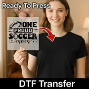 A smiling woman holding a sign with the text "ONE PROUD SOCCER MOM" and a red arrow pointing to her chest.