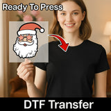 A smiling woman in black holds an InkMerge Funny Santa Star Sunglasses transfer, with a red arrow pointing to her shirt. "Ready To Press" appears above and "DTF Transfer—perfect for the holiday season" below.