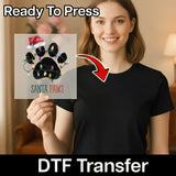 A woman in a black shirt holds the InkMerge Santa Paws Christmas DTF Transfer—an 8-pass pre-cured, ready-to-press sheet featuring a paw print with Christmas lights and a Santa hat. Text reads "Ready to Press" and "DTF Transfer.