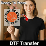 A woman holding a basketball-themed sign with the text "Court My Heart Is Not on the Court" and a red arrow pointing to her chest.