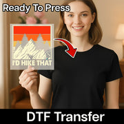 A smiling woman in a black shirt holds a square DTF transfer by InkMerge featuring mountains, trees, and the quote "The Mountains Are Calling Adventure Quote." An arrow points to her shirt. Text reads “Ready To Press” & “DTF Transfer.”.