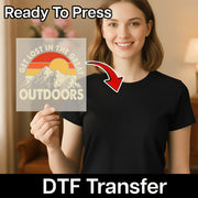 A woman in a black shirt holds an InkMerge Take A Hike Retro Mountain Sunset DTF transfer with a sunset, mountains, and text. An arrow points at her shirt. "Ready To Press—a perfect design for your next heat press project" appears above.