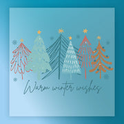The Warm Winter Wishes Vintage Design by InkMerge features six colorful, stylized Christmas trees on a blue, snowflake background with “Warm winter wishes” below in elegant script, perfect for retro garment transfers.