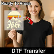 A smiling woman in a black t-shirt holds a transparent InkMerge DTF film featuring a Take A Hike Retro Sunset Design. Text says Ready To Press and Heat Press Transfer, with a red arrow pointing to her shirt.