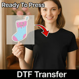 A smiling woman in a black shirt holds a transparent sheet featuring InkMerge's Quirky Skull Christmas Stocking Design, ideal for ugly sweater parties. "Ready To Press" appears at the top, "DTF Transfer" at the bottom, with a red arrow pointing to the design.