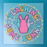 a colorful, circular design with the text "Teaching some bunny" written around it. The design includes a pink bunny, a purple bunny, and a blue bunny, all set against a blue background with a pattern of colorful squares.