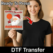 A smiling woman in a black shirt holds the InkMerge “Santa's Favorite Basketball” DTF transfer, featuring Santa spinning a basketball with “Ready To Press” above and “DTF Transfer” below—perfect for custom apparel.