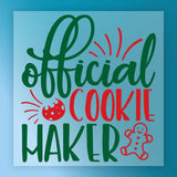 The Cookie Maker Festive Design by InkMerge features "official cookie maker" in green and red with a bitten cookie and smiling gingerbread man on a blue festive background—ideal for DTF or precut heat transfer projects.