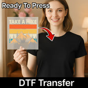 A smiling woman in a black shirt holds an InkMerge Retro Mountain Sunset Design - Heat Press Ready sheet. Text above reads Ready To Press, and below reads DTF Transfer, perfect for your next heat press project.