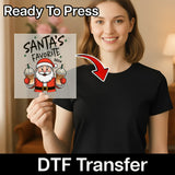 A smiling woman in a black shirt holds InkMerge's Santa's Favorite Brew Funny Christmas Design DTF transfer. Text reads Ready To Press and DTF Transfer with a red arrow—ideal for your holiday heat press projects!.