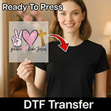 A smiling woman in a black shirt holds InkMerge's Peace Love Jesus Design premium DTF film, featuring peace sign, heart, and cross symbols. Text reads "Ready To Press" and heat press transfer.