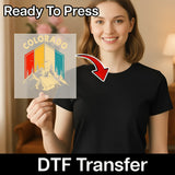 A smiling woman in a black shirt holds InkMerge’s Tropical Palm Tree Silhouette Colorado DTF transfer, featuring vibrant mountains and tropical style. An arrow points to her shirt with “Ready To Press” and “DTF Transfer” text.