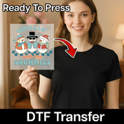 A woman in a black shirt holds the InkMerge "Chillin' With My Snowmies Design" transfer sheet, featuring three cartoon snowmen. An arrow highlights her shirt. Text above reads “Ready To Press,” below: “DTF transfers for custom apparel.”.