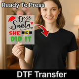 A smiling woman in a black shirt holds the InkMerge Dear Santa SHE DID IT Holiday Humor DTF transfer sheet, featuring festive red, green, and black lettering—perfect for adding holiday cheer with your heat press.