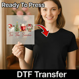 A smiling woman in a black shirt holds an InkMerge “Tis The Season Vintage Christmas” DTF transfer sheet featuring Santa, a tree, and holiday icons. Ready To Press—perfect for festive garment printing.