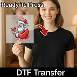 A smiling woman in a black t-shirt holds a transparent DTF sheet with InkMerge's Whispers of Winter Santa & Cardinal Design – Heat Press Ready. Text on the image reads "Ready To Press" and "holiday heat press DTF Transfer.