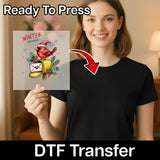 A smiling woman in a black shirt holds an InkMerge Winter Messenger Cardinal Christmas Design DTF transfer sheet with cardinal, yellow bell, holly, and “WINTER MESSENGER” text—Ready To Press and perfect for your heat press projects.
