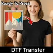 A smiling woman in a black shirt holds an “Abstract Mountain Adventure” DTF transfer by InkMerge with a colorful mountain and sun design. “Ready To Press” is above, “DTF Transfer” below, and an arrow points from the sheet to her shirt.