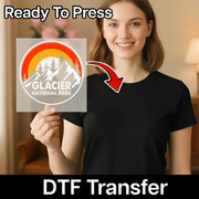 A smiling woman in a black shirt holds a clear sheet featuring the Retro Mountain Rainbow Adventure - Heat Press Ready design by InkMerge. "Ready To Press" is at the top, with "InkMerge DTF transfers" at the bottom and a red arrow pointing to the sheet.