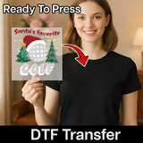 A smiling woman in a black t-shirt holds an InkMerge "Santa's Favorite Golf Xmas Design" DTF transfer sheet, featuring Santa’s hat, golf ball, and Christmas trees. Text above says Ready To Press—ideal for your next heat press project!.