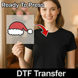 A smiling woman in a black shirt holds the InkMerge Santa Hat Christmas Cheer DTF transfer—an easy, Ready To Press design perfect for custom holiday apparel.