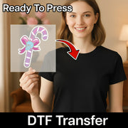A woman in a black t-shirt holds a transparent DTF transfer sheet with the InkMerge Gothic Candy Cane Skull Design featuring a pink bow. A red arrow points to her shirt. Text: “Ready To Press” and “DTF Transfer—perfect for custom apparel.”.