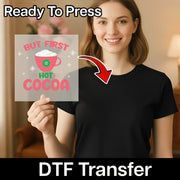 A smiling woman in a black shirt holds the InkMerge "But First Hot Cocoa Design" DTF transfer sheet. An arrow points from the festive sheet to her shirt, with text: Ready To Press and custom shirt transfers.