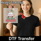 A smiling woman in a black shirt holds an InkMerge Holiday Shirt Design DTF transfer sheet with a festive car, Santa, and Christmas tree—perfect for custom holiday apparel with your heat press. Ready To Press!.