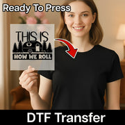 A smiling woman in a black t-shirt holds InkMerge’s "This Is How We Roll Camper Design - Heat Press Ready" DTF transfer sheet, perfect for your next heat press project.
