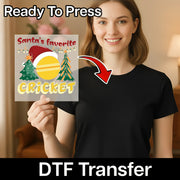 A smiling woman in a black shirt holds an InkMerge DTF transfer sheet with the Santa's Favorite Cricket Holiday Design—featuring a Santa hat, cricket ball, Christmas trees, and festive lights. Ready To Press DTF Transfer for heat press projects.