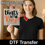 A smiling woman holding a sign with the text "That's my boy!" in front of her.