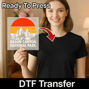 A smiling woman in a black t-shirt holds an InkMerge Retro Desert Sunset Adventure DTF transfer with the Grand Canyon and a sunset, labeled "Ready To Press"—perfect for your next direct-to-film heat press project.
