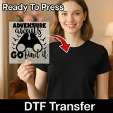 A woman in a black shirt holds the InkMerge Adventure Awaits Go Find It Design, a screen printing alternative for custom apparel transfers with “Adventure awaits, go find it” text and binoculars graphic. An arrow points to the sheet.