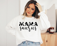 A woman smiling and wearing a white long-sleeved sweatshirt with the text 'MAMA saurus' in black font.