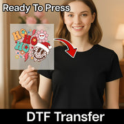 A smiling woman holds an InkMerge HO HO HO Festive Design DTF transfer sheet with a vibrant holiday theme in front of her black shirt. "Ready To Press" and "DTF Transfer" text highlight the precut heat press transfer.