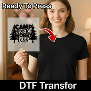 A woman in a black shirt smiles, holding InkMerge’s transparent "Camp More Worry Less Silhouette Design" DTF transfer—ideal for heat press projects. An arrow points to her shirt’s design. Text above reads “Ready To Press.”.