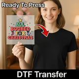 A smiling woman in a black tee holds an InkMerge All Booked For Christmas Funny Design DTF transfer sheet with festive decor. “Ready To Press” tops the sheet, “DTF Transfer” is below—a perfect holiday shirt print!.