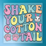 the text "SHAKE YOUR COTTON TAIL" in a colorful, whimsical font, with a bunny's head and paw prints below the text.