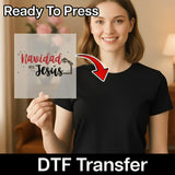 A smiling woman in a black shirt holds the InkMerge "Navidad Es Jesús Religious Design" DTF transfer sheet with festive graphics. An arrow points to her shirt. Text above says "Ready To Press," highlighting this holiday heat press transfer.