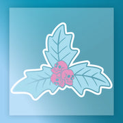 The InkMerge "Gothic Pink Skulls on Holly" transfer features two crossed blue leaves and three pink skulls at their intersection, set on a blue background with a white border—ideal for adding bold, custom flair to your apparel.