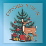 A deer stands before a decorated tree with red ornaments and gifts. "CHRISTMAS IN THE AIR" appears above on blue—perfect for festive shirts or DTF transfers. Product: Christmas In The Air Festive Scene - Heat Press Ready by InkMerge.