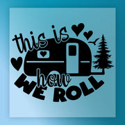 a black and white graphic design with a camper trailer, hearts, and a pine tree. The text "This is how we roll" is prominently displayed in the center of the image.