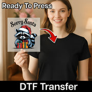A woman in a black shirt holds InkMerge's "Sorry Santa Raccoon Holiday Humor" DTF Transfer for heat press, showing a cartoon raccoon in a Santa hat. An arrow points from the transfer sheet to her shirt. Text reads Ready To Press.