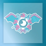 The InkMerge Gothic Pastel Skull Wreath showcases a central eye, blue bat wings, pink skulls, candy canes, and holly leaves with a pink bow on a blue gradient—ideal for DTF transfers.