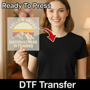 A smiling woman in a black shirt holds the InkMerge “Adventure Awaits Retro Mountain Design - Heat Press Ready” DTF transfer featuring a retro mountain and sunset graphic. An arrow points to her shirt with text: “Ready To Press,” “DTF Transfer,” and “custom apparel.”.